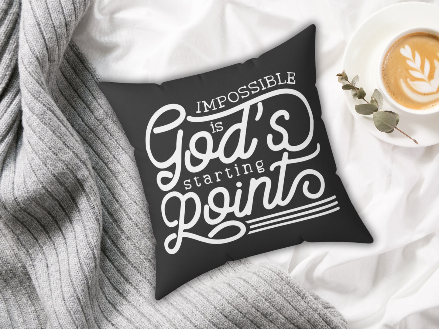Black pillow with motivational quote on a white surface with a cup of coffee and plant.