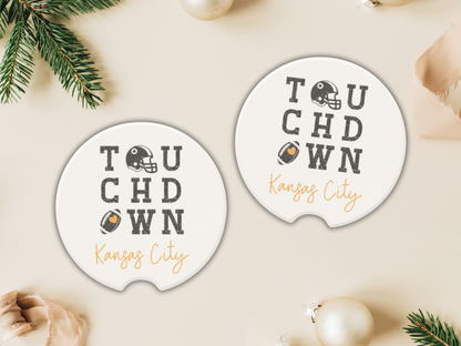 Two 'Touchdown Kansas City' coasters on a beige surface with Christmas decorations.