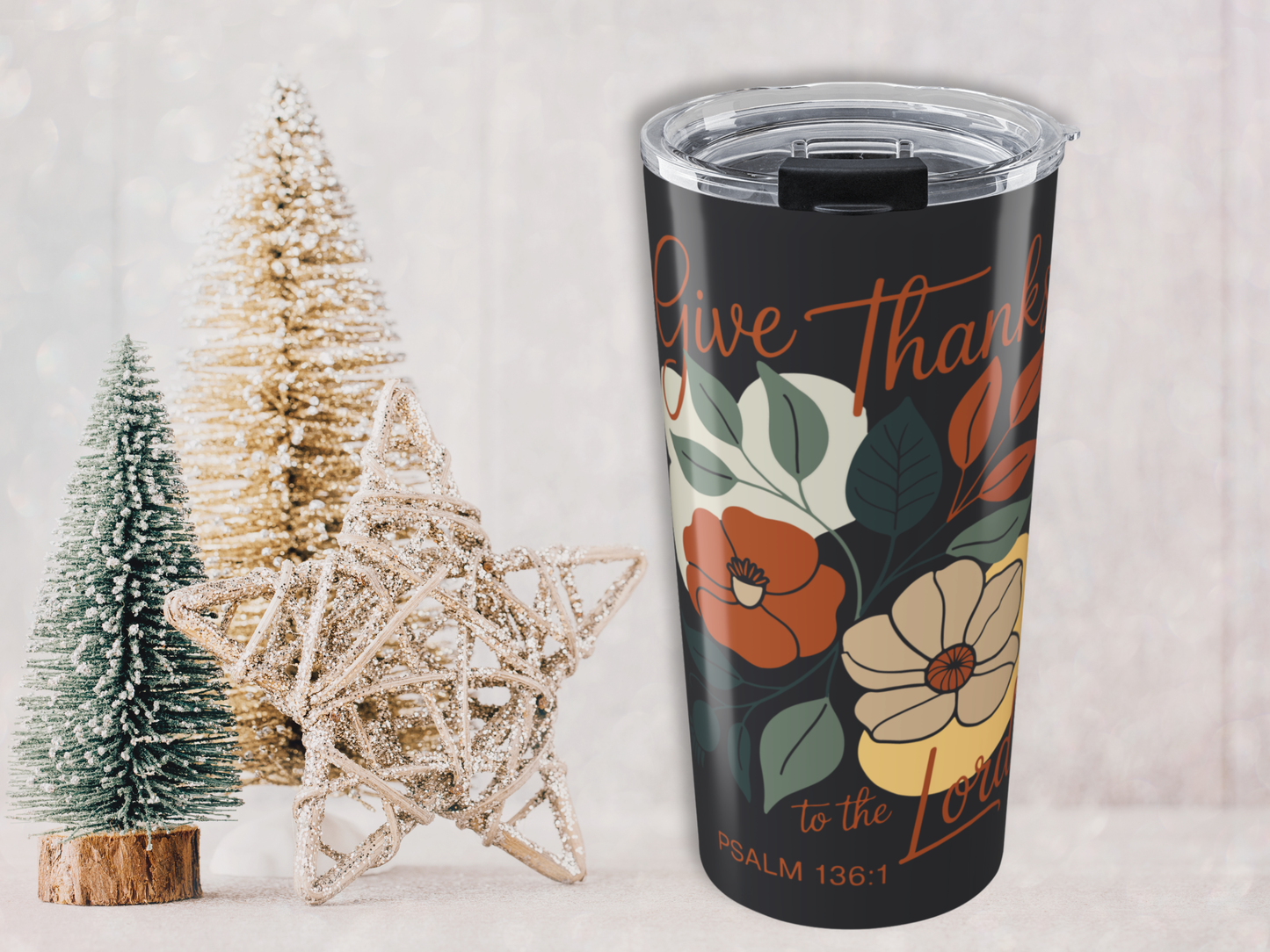 Tumbler with floral design and text next to decorative Christmas trees on a light background