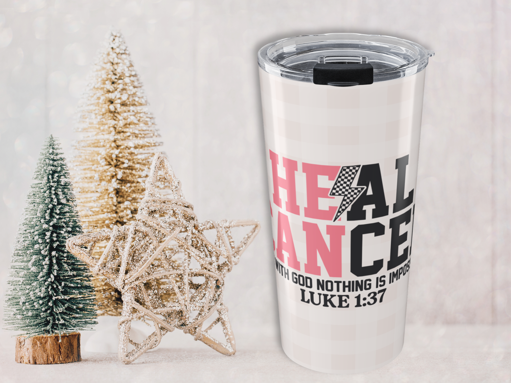 Pink plaid tumbler with motivational quote next to decorative Christmas trees on a light background