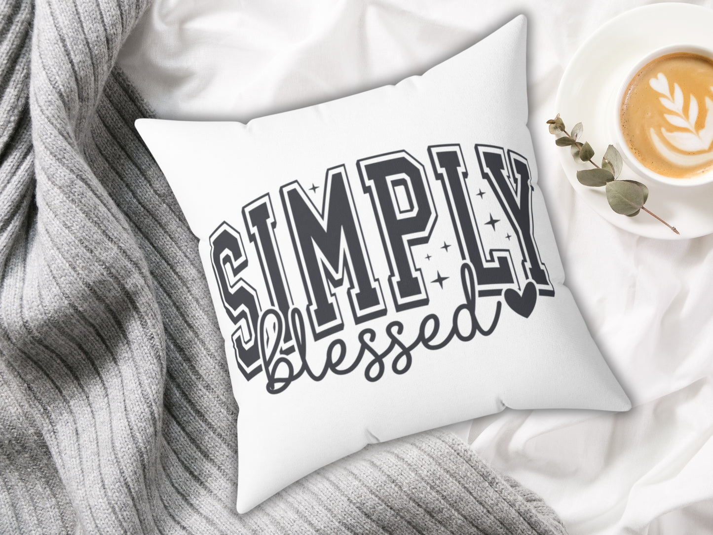 White pillow with 'Simply Blessed' text on a soft fabric background with a cup of coffee.