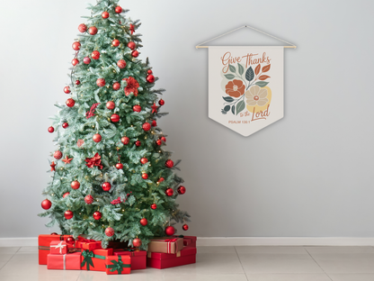 Decorated Christmas tree with red ornaments and presents, next to a wall hanging with 'Give Thanks' text.
