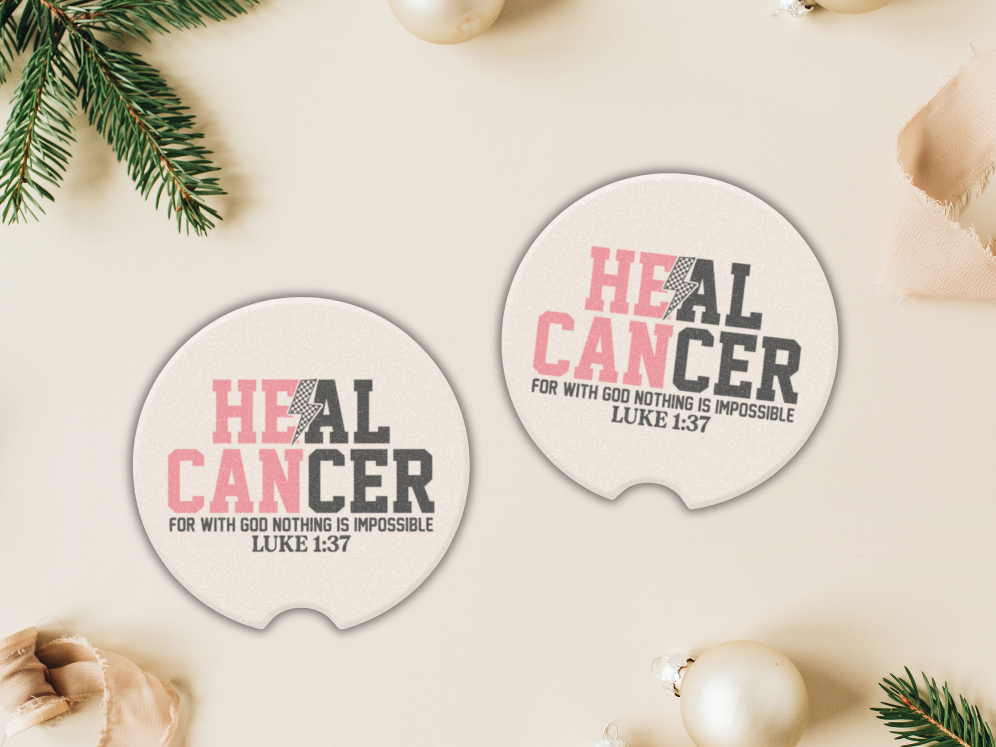 Two circular 'Heal Cancer' car coasters on a light surface with Christmas decorations.