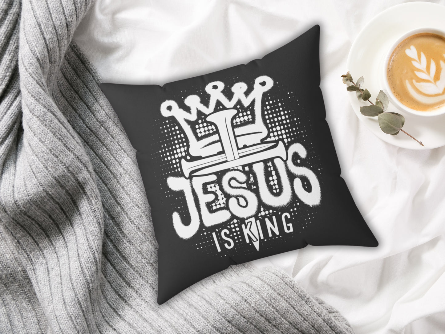 Black pillow with 'Jesus is King' design on a white surface with a cup of coffee.