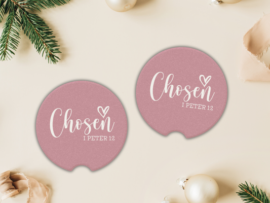 Pink coasters with 'Chosen 1 Peter 1:2' text on a beige surface with Christmas decorations.