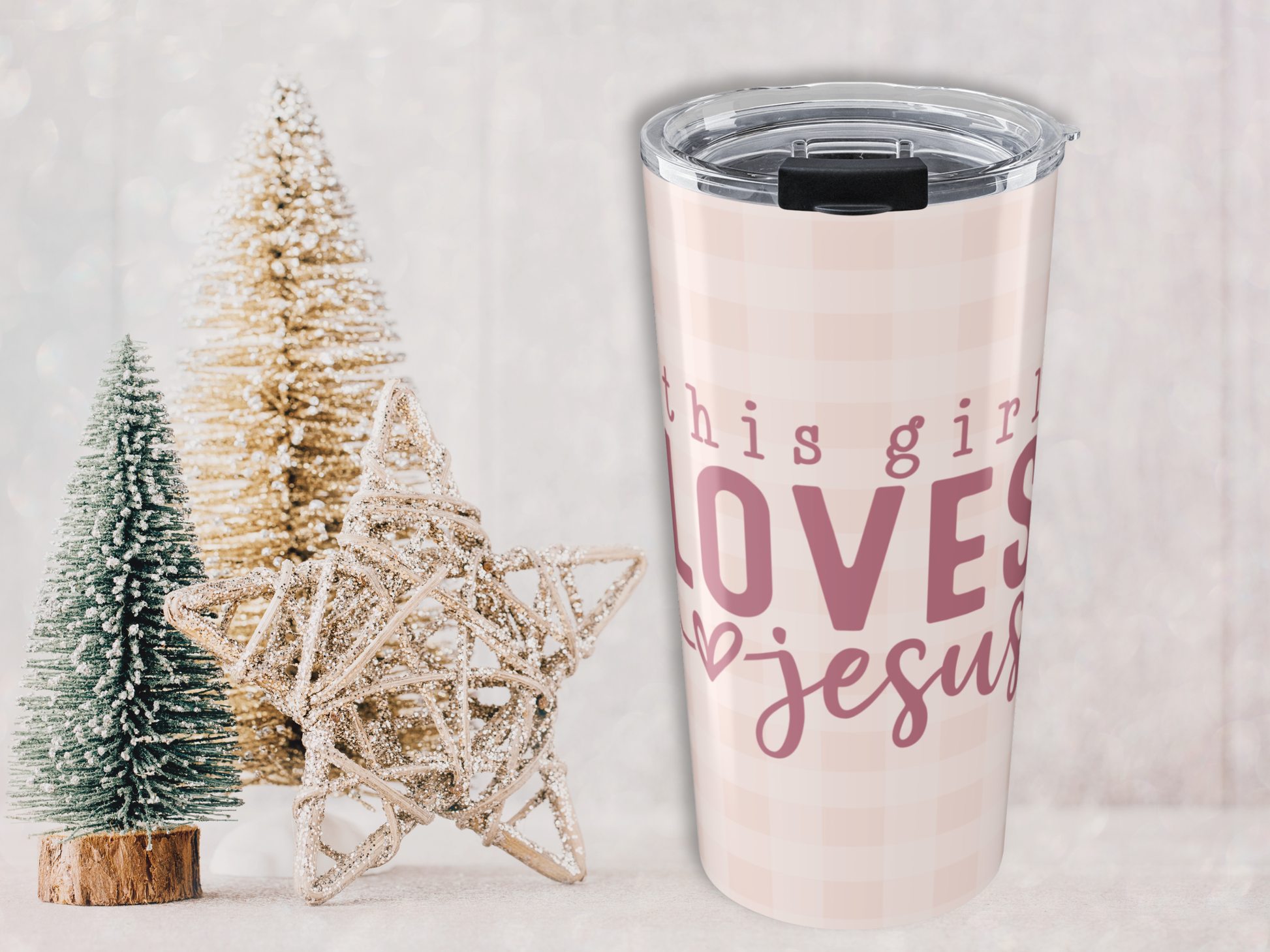 Tumbler with 'this girl loves Jesus' text next to Christmas trees on a light background