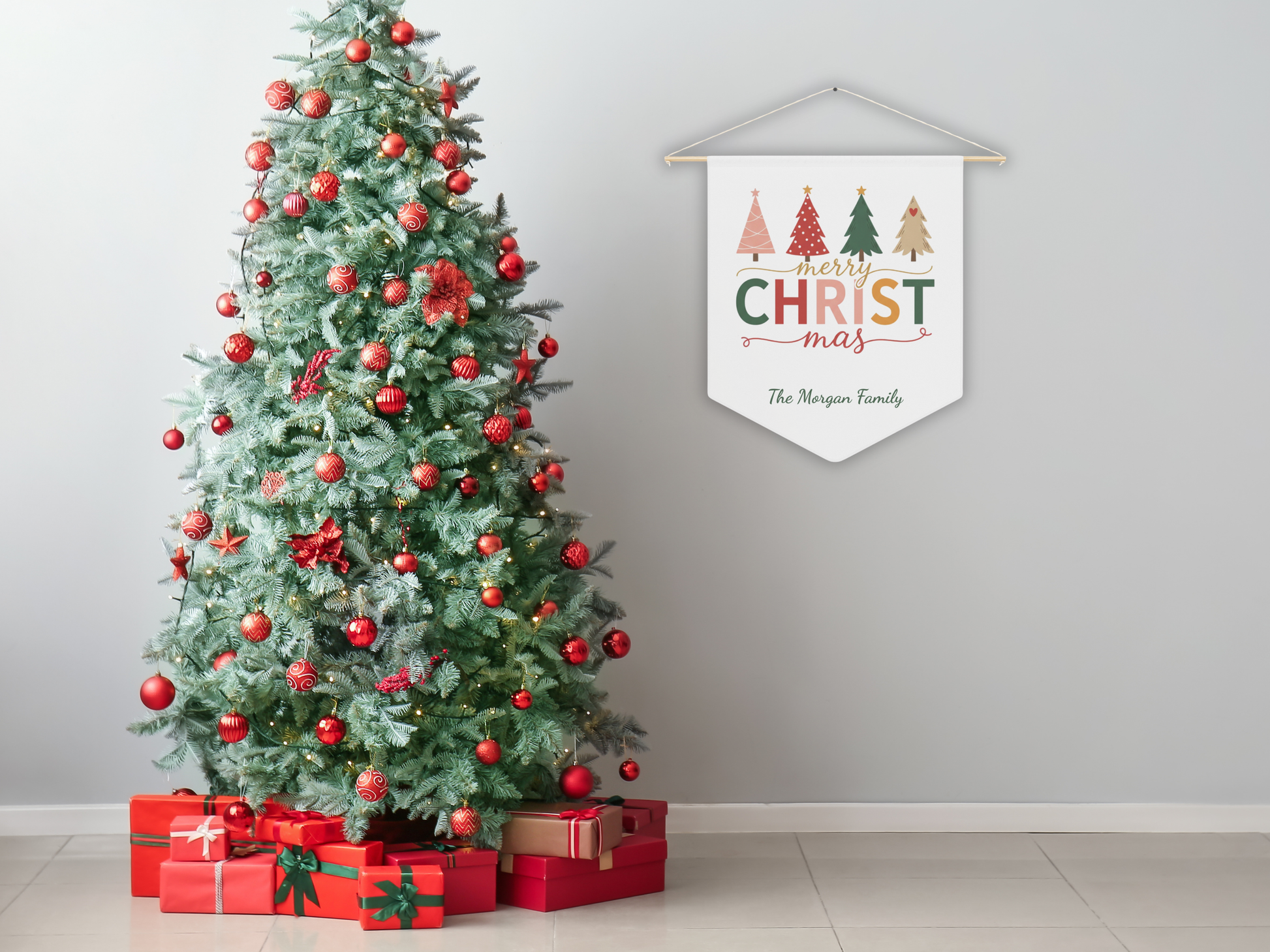 Decorated Christmas tree with red ornaments and presents, next to a 'Merry Christmas' banner on a plain wall.