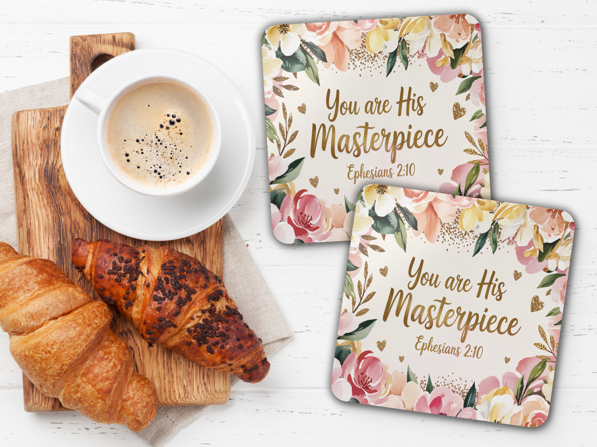 Two floral “You are His Masterpiece” coasters styled with a cup of coffee, wooden board, and croissants on a white table.