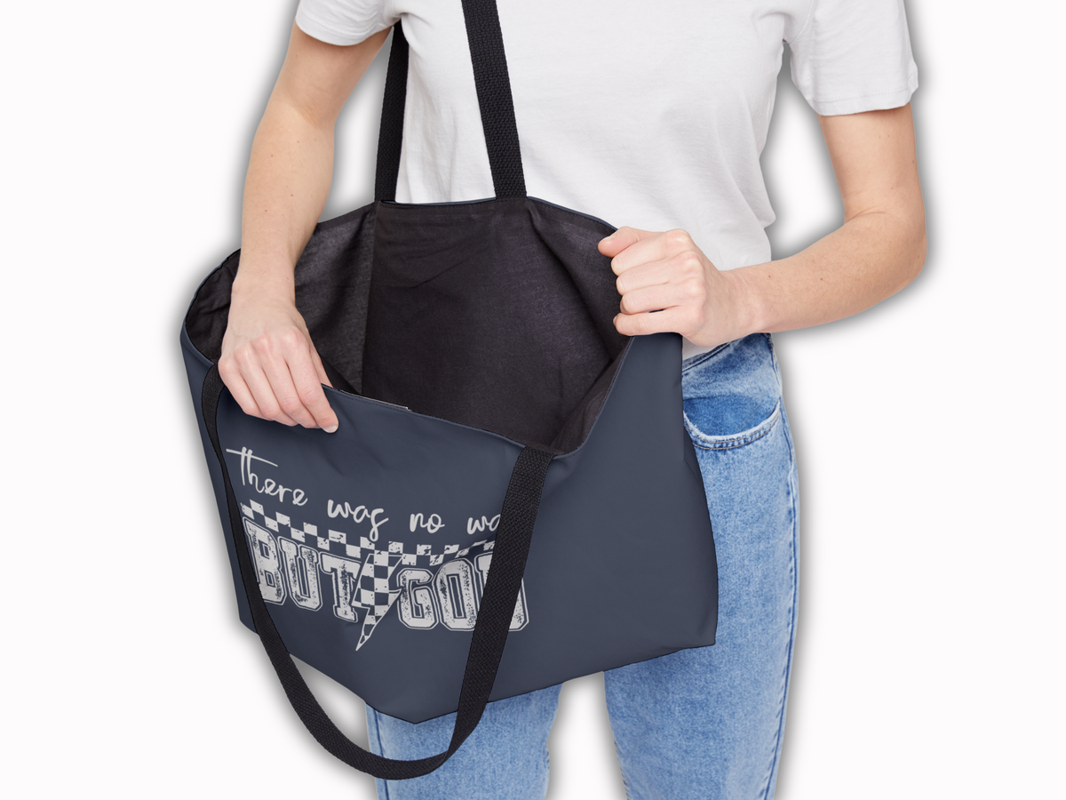 Woman in white shirt and jeans holding open navy tote bag with black interior lining, showing spacious design and “There was no way BUT GOD” print.