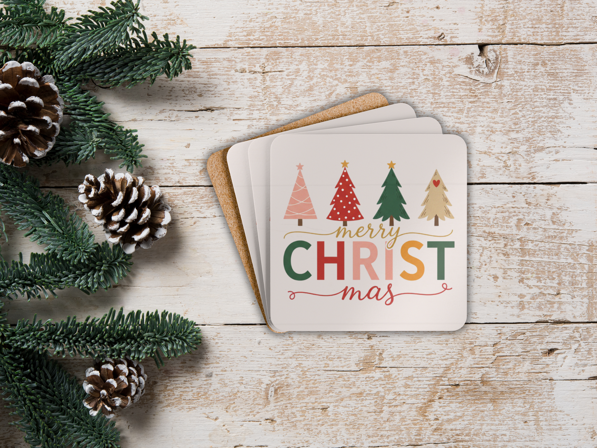 Coasters with Christmas design on a wooden surface with pine cones and greenery.