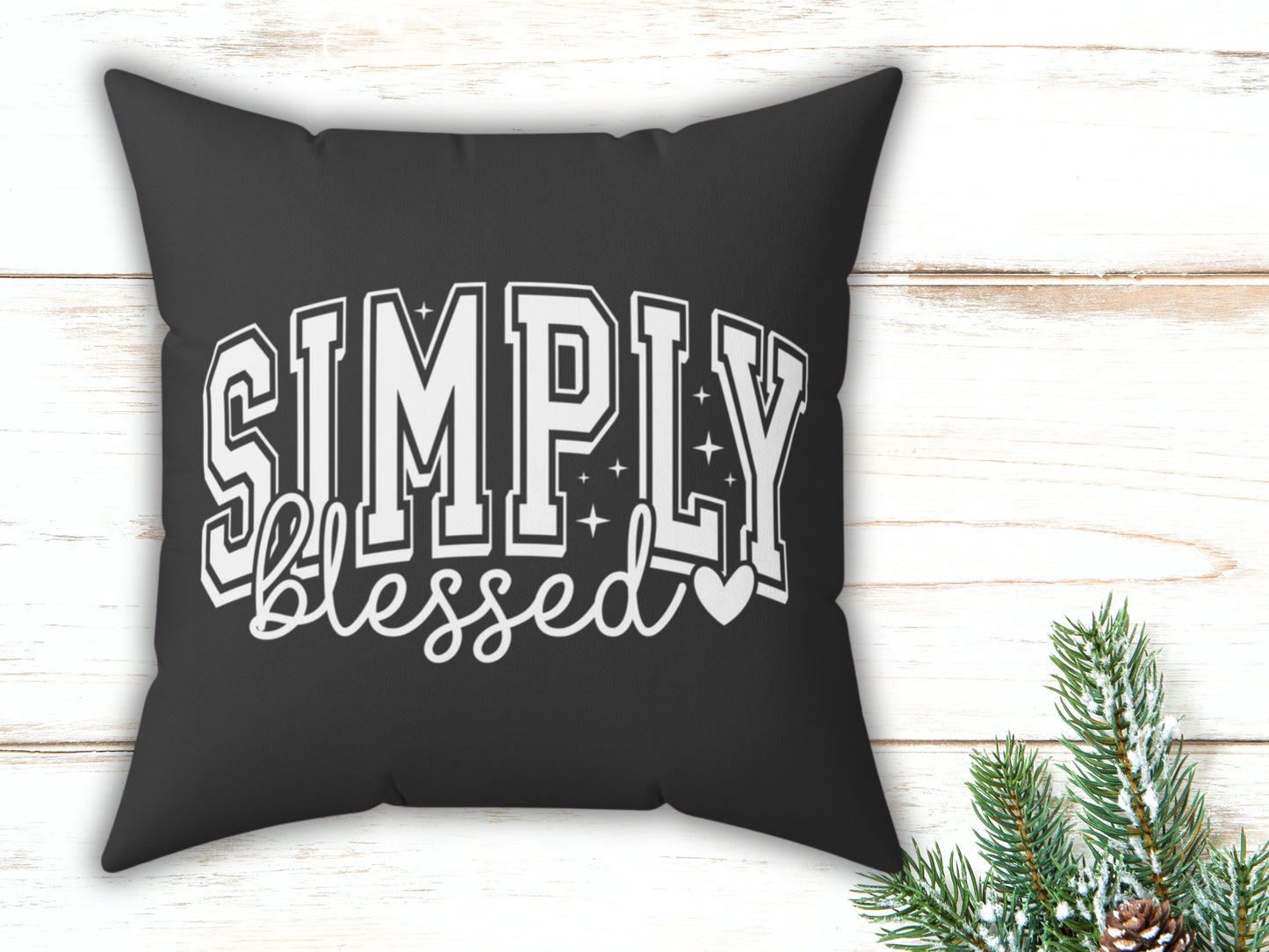 Black pillow with 'Simply blessed' text on a wooden surface with Christmas decorations.