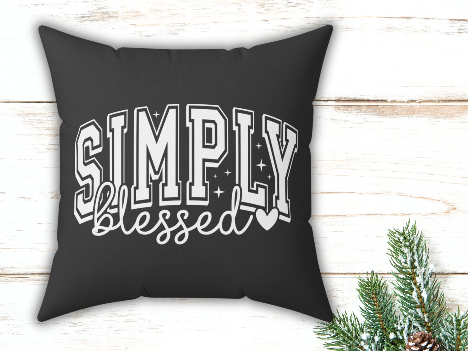 Black pillow with 'Simply blessed' text on a wooden surface with Christmas decorations.