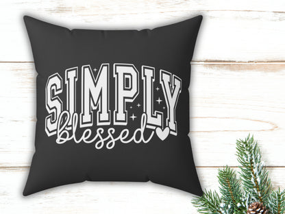 Black pillow with 'Simply blessed' text on a wooden surface with Christmas decorations.
