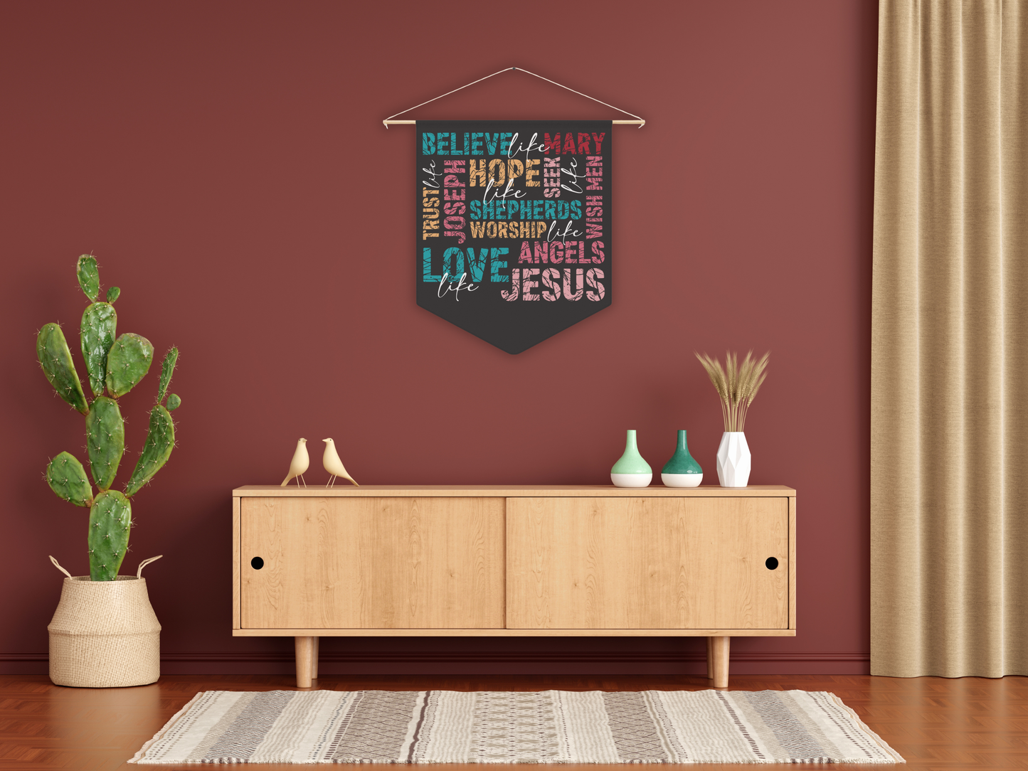 Decorative wall hanging with text above a wooden cabinet in a room with a plant and curtains.