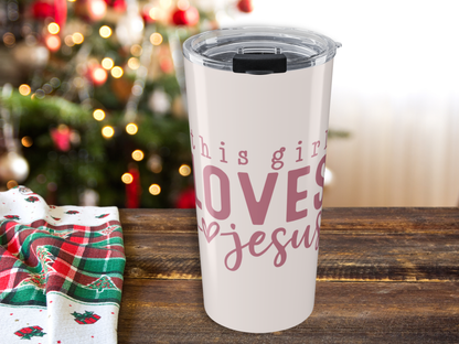 Pink tumbler with 'This girl loves Jesus' text on a wooden table with a Christmas tree in the background.
