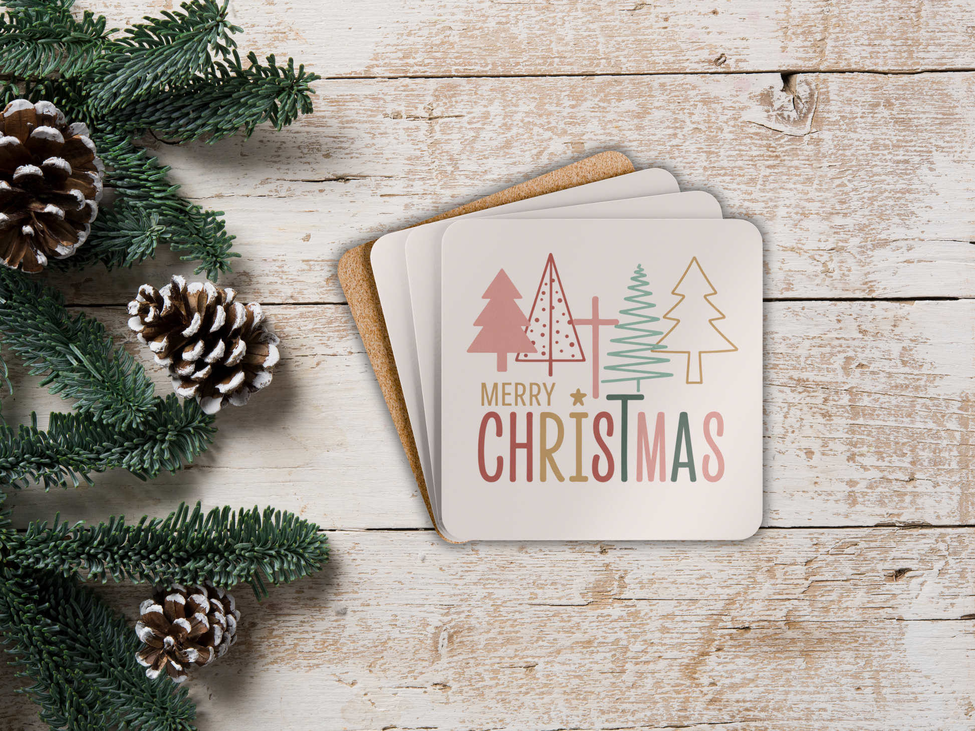 Stack of Christmas cards with decorative trees and 'Merry Christmas' text on a wooden surface with pine cones and greenery.