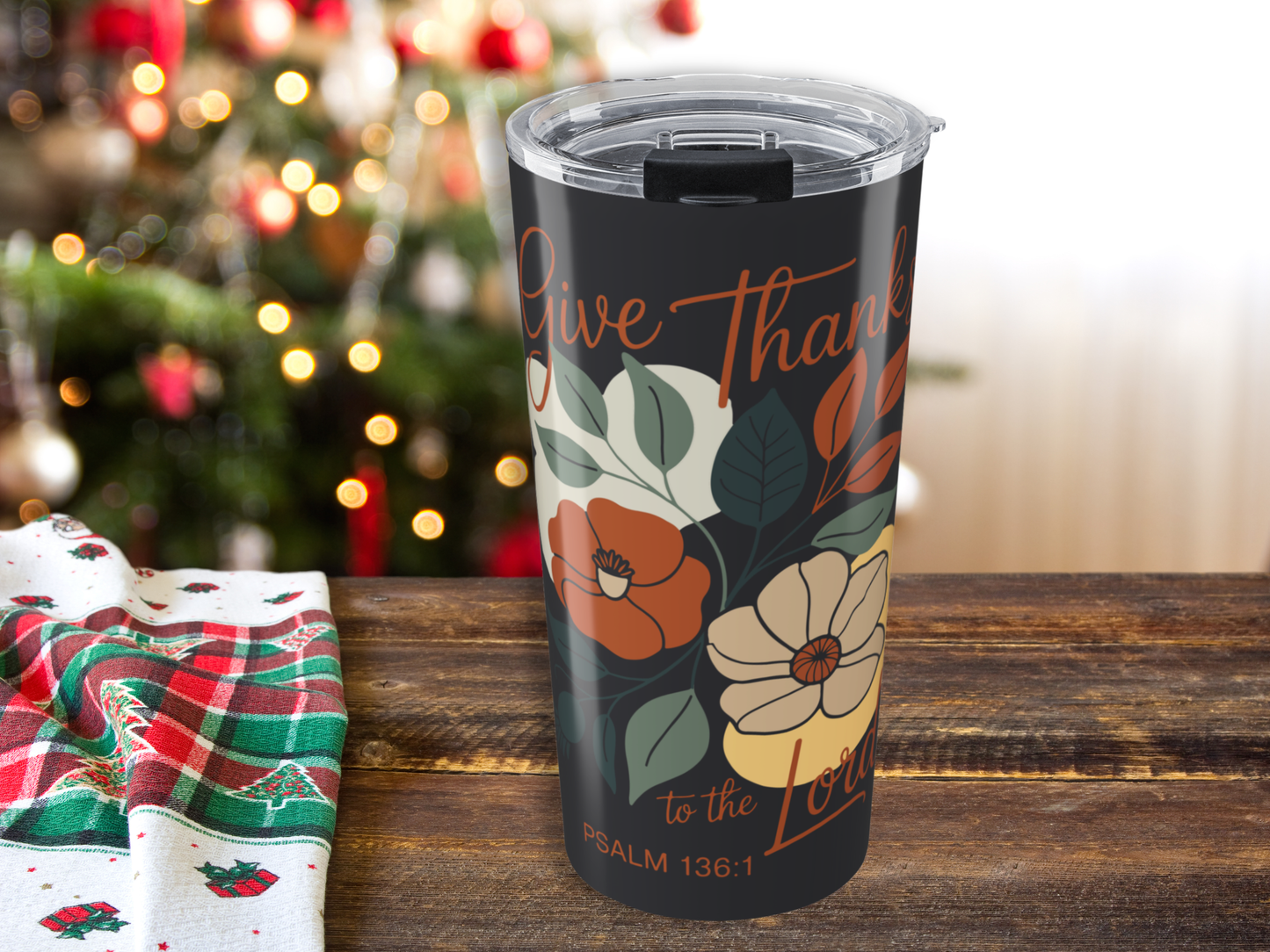 Tumbler with floral design and text on a wooden table with a Christmas tree in the background