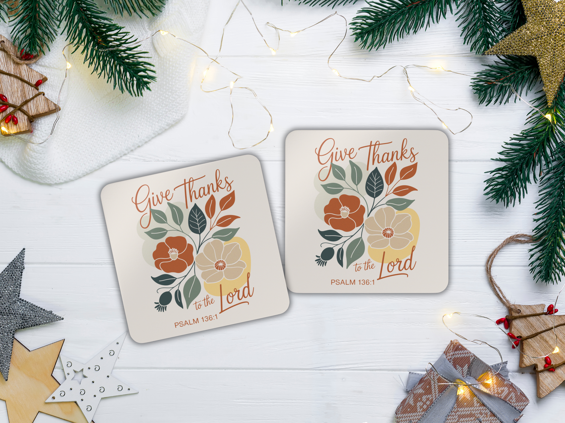 Two coasters with floral designs and text on a white surface with Christmas decorations.