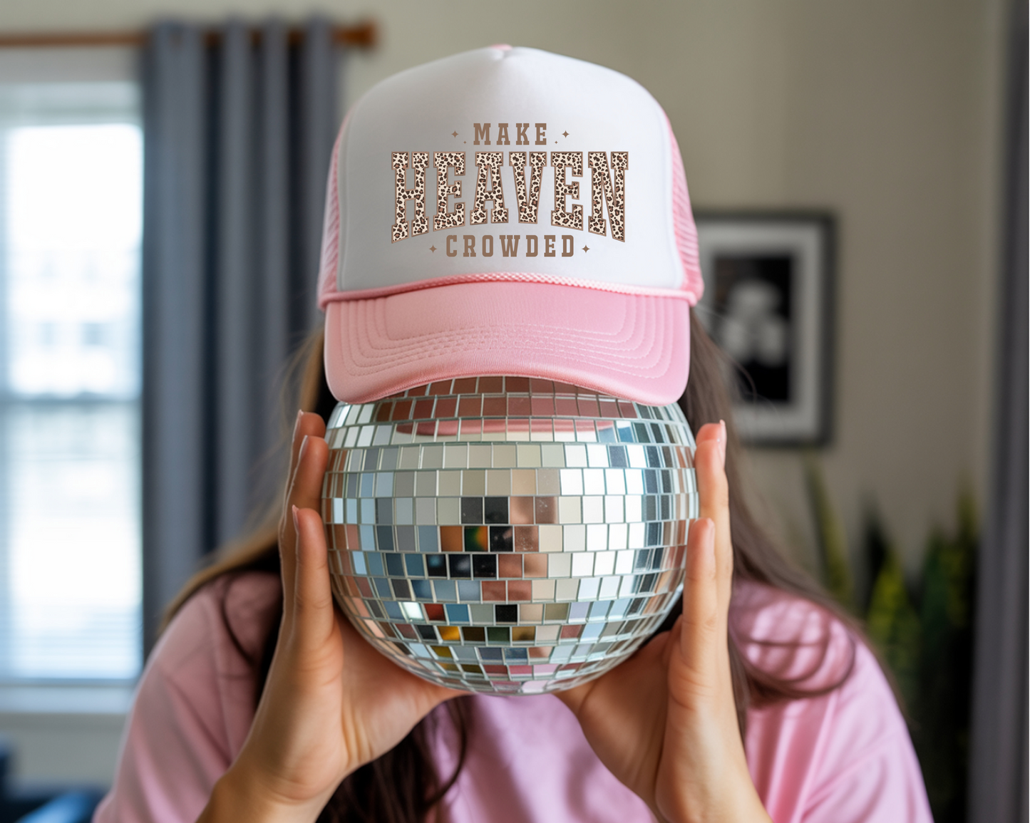 Person holding a disco ball wearing a pink and white cap with text.