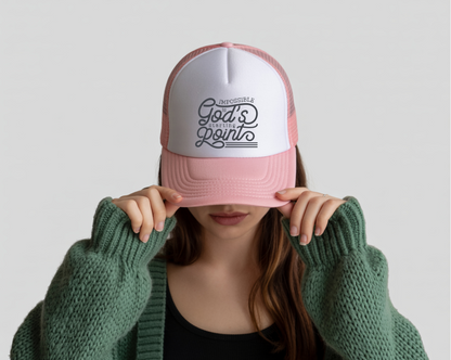 Person wearing a pink and white cap with text, holding it over their face against a light gray background