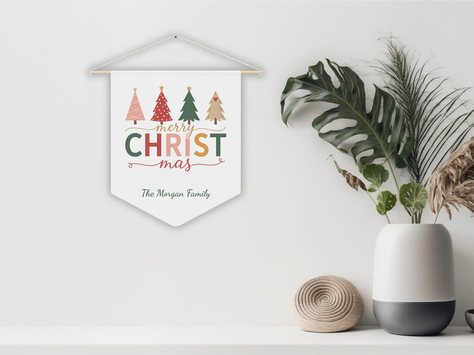 Decorative Christmas banner with colorful trees on a white wall, next to a plant and vase.