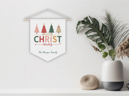 Decorative Christmas banner with colorful trees on a white wall, next to a plant and vase.