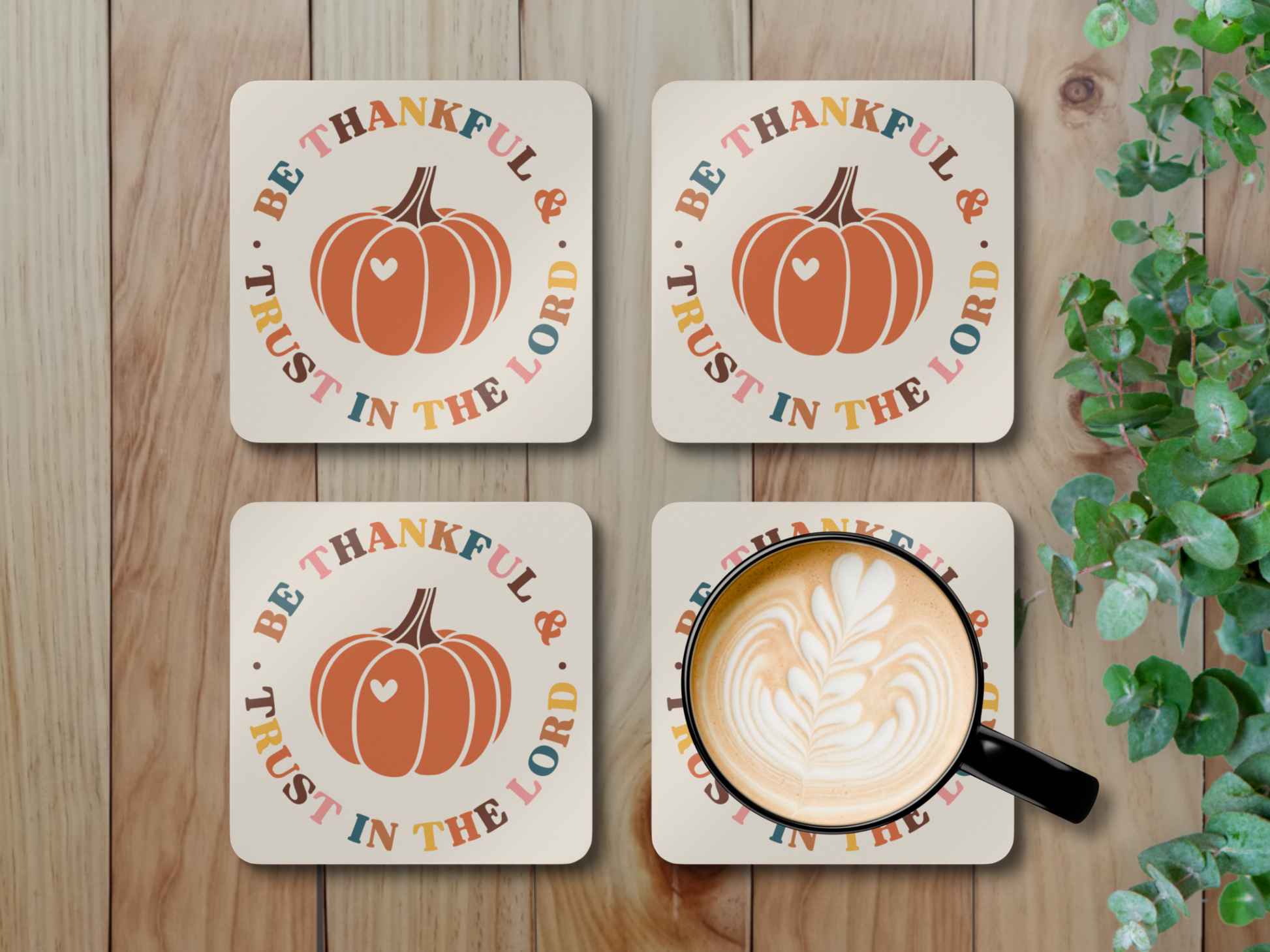 Four Christian pumpkin coasters with latte mug styled on rustic wood surface with leafy greenery.