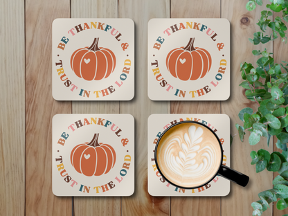 Four Christian pumpkin coasters with latte mug styled on rustic wood surface with leafy greenery.