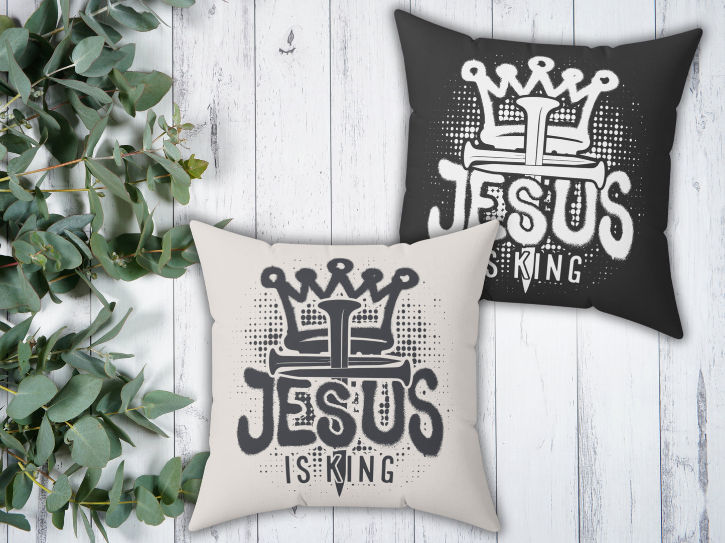 Two pillows with 'Jesus is King' design on a wooden surface with greenery.