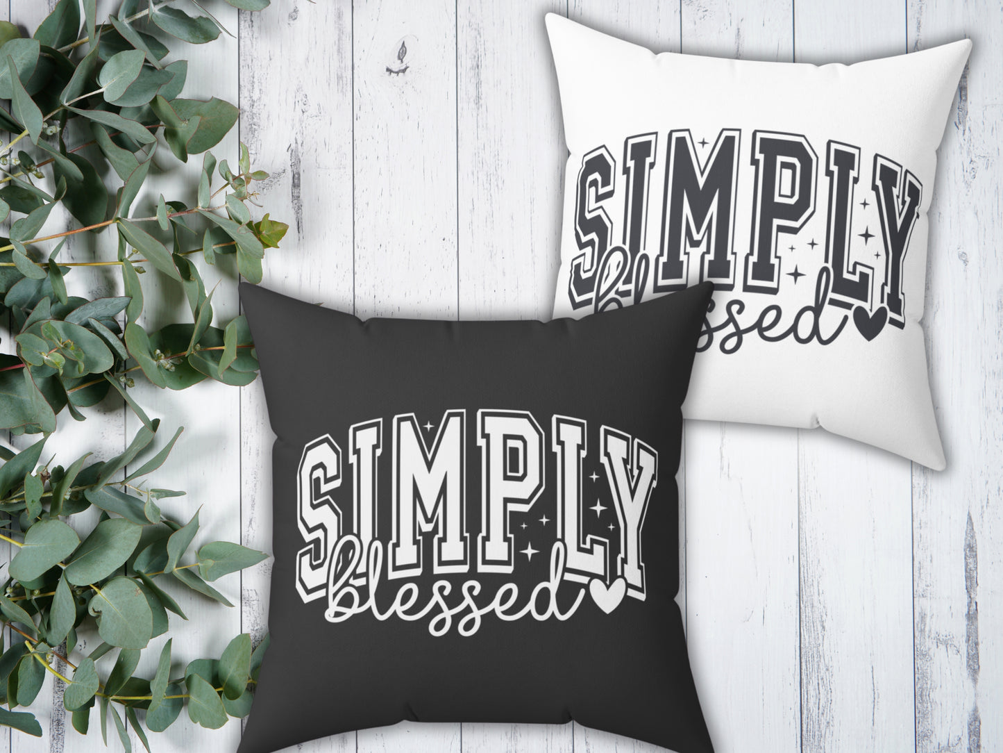 Two pillows with 'Simply Blessed' text on a wooden surface with greenery.
