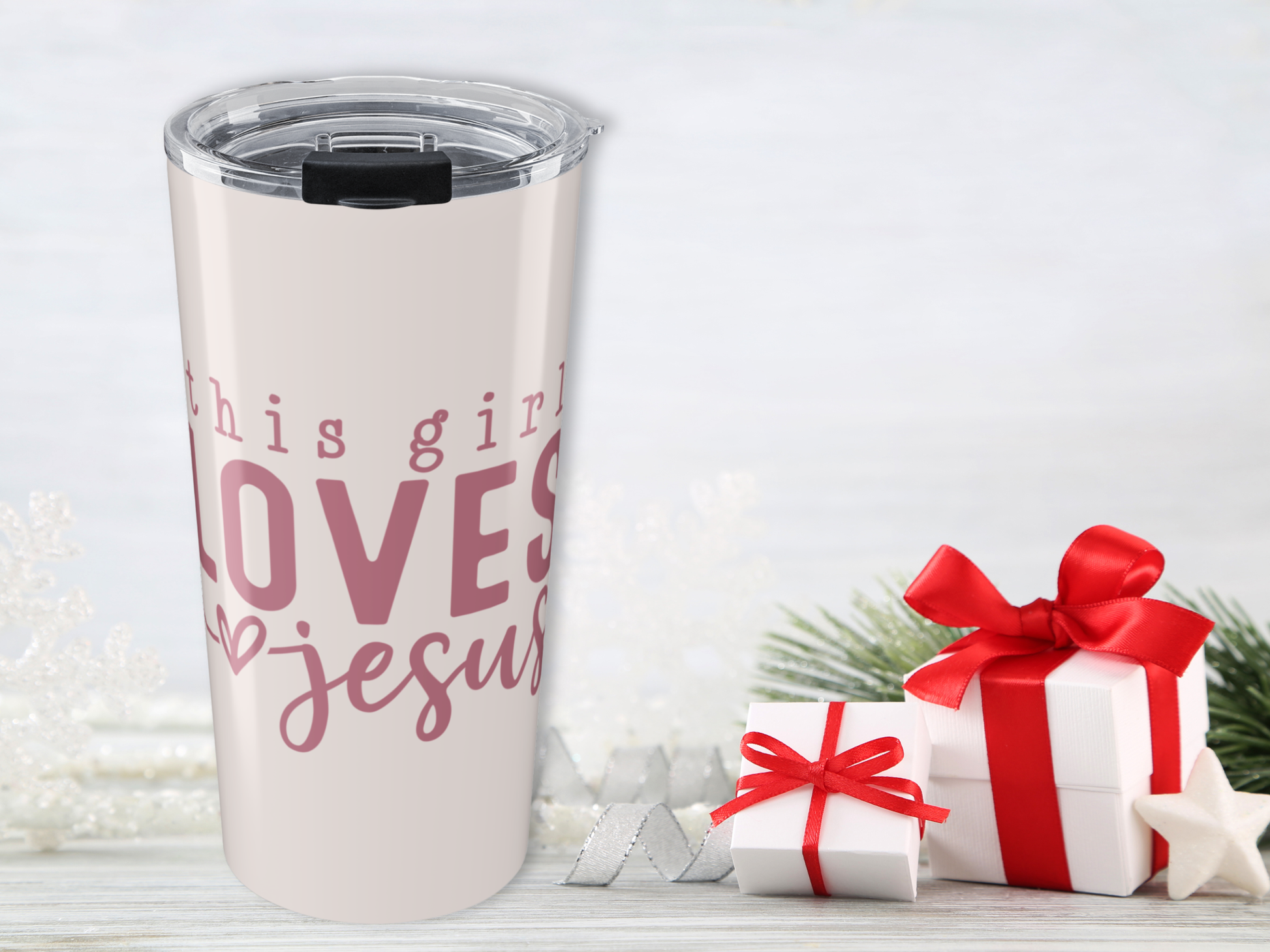 Tumbler with 'This girl loves Jesus' text next to gift boxes on a light background