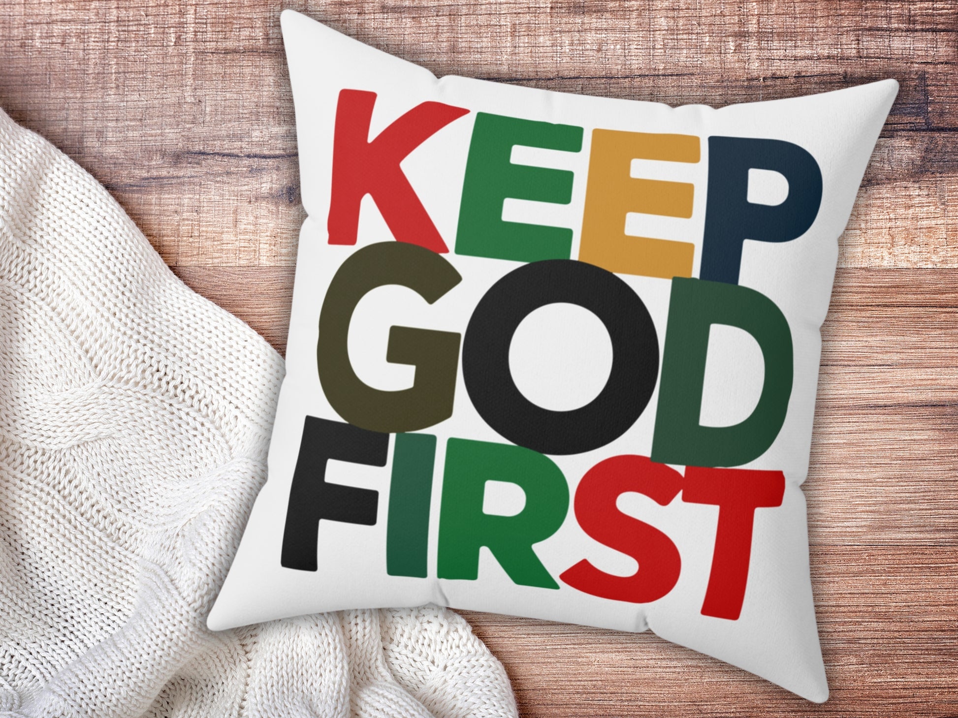White pillow with colorful text 'KEEP GOD FIRST' on a wooden surface.