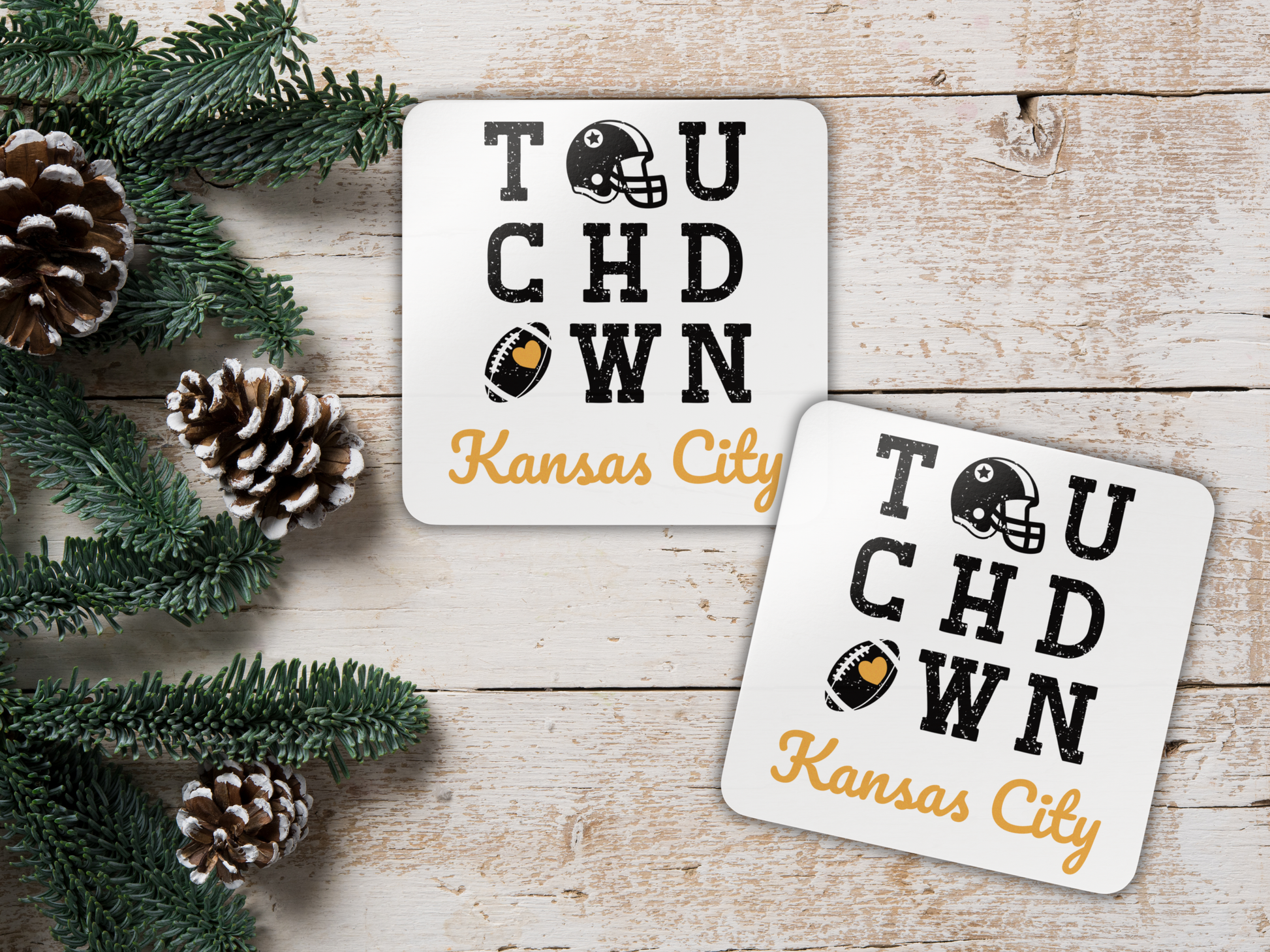 Two 'Touchdown Kansas City' coasters on a wooden surface with pine cones and greenery.