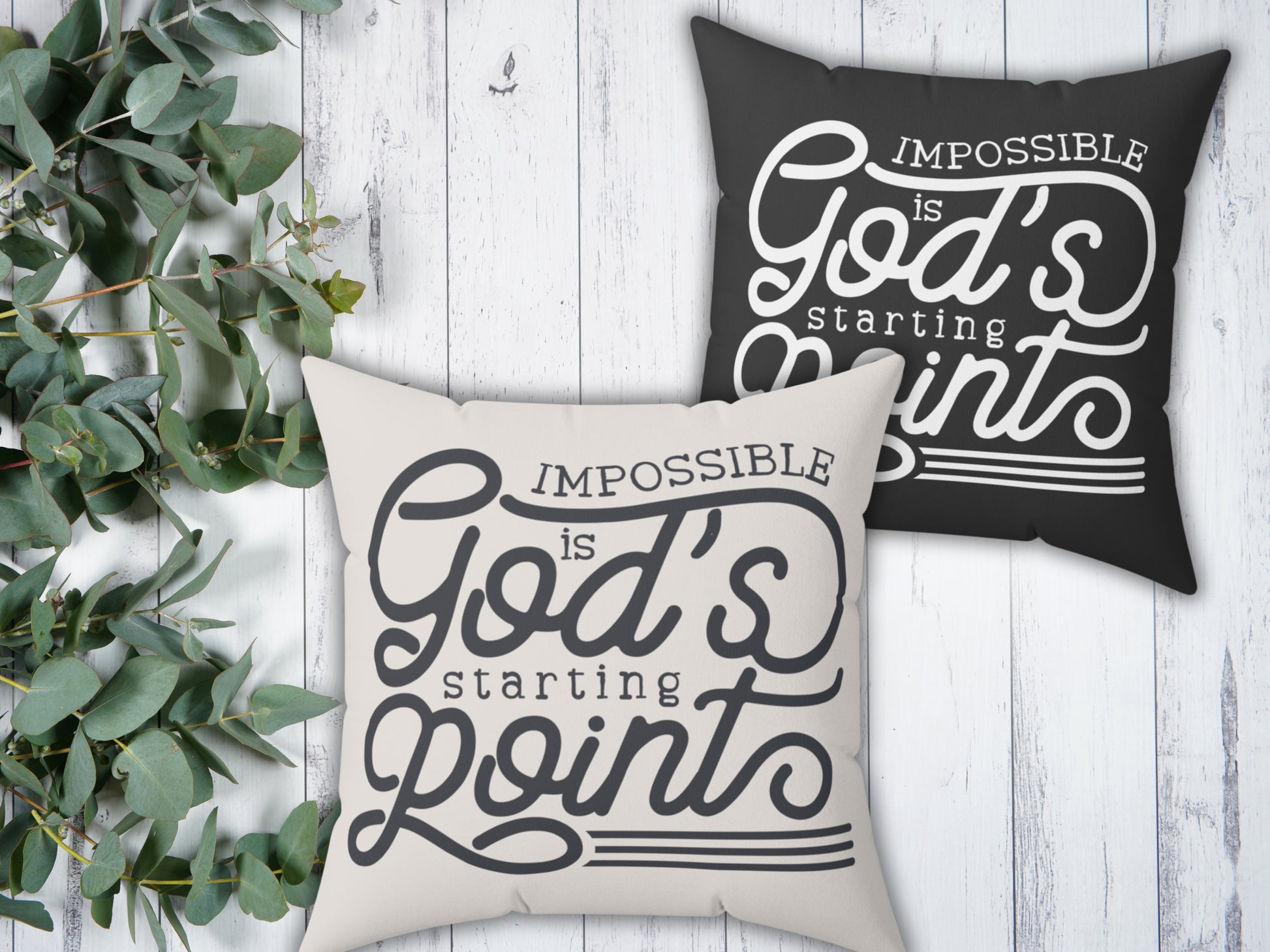 Two pillows with motivational phrases on a wooden surface with greenery.