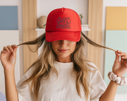 Person wearing a red cap with text, holding hair in a room with colorful walls.