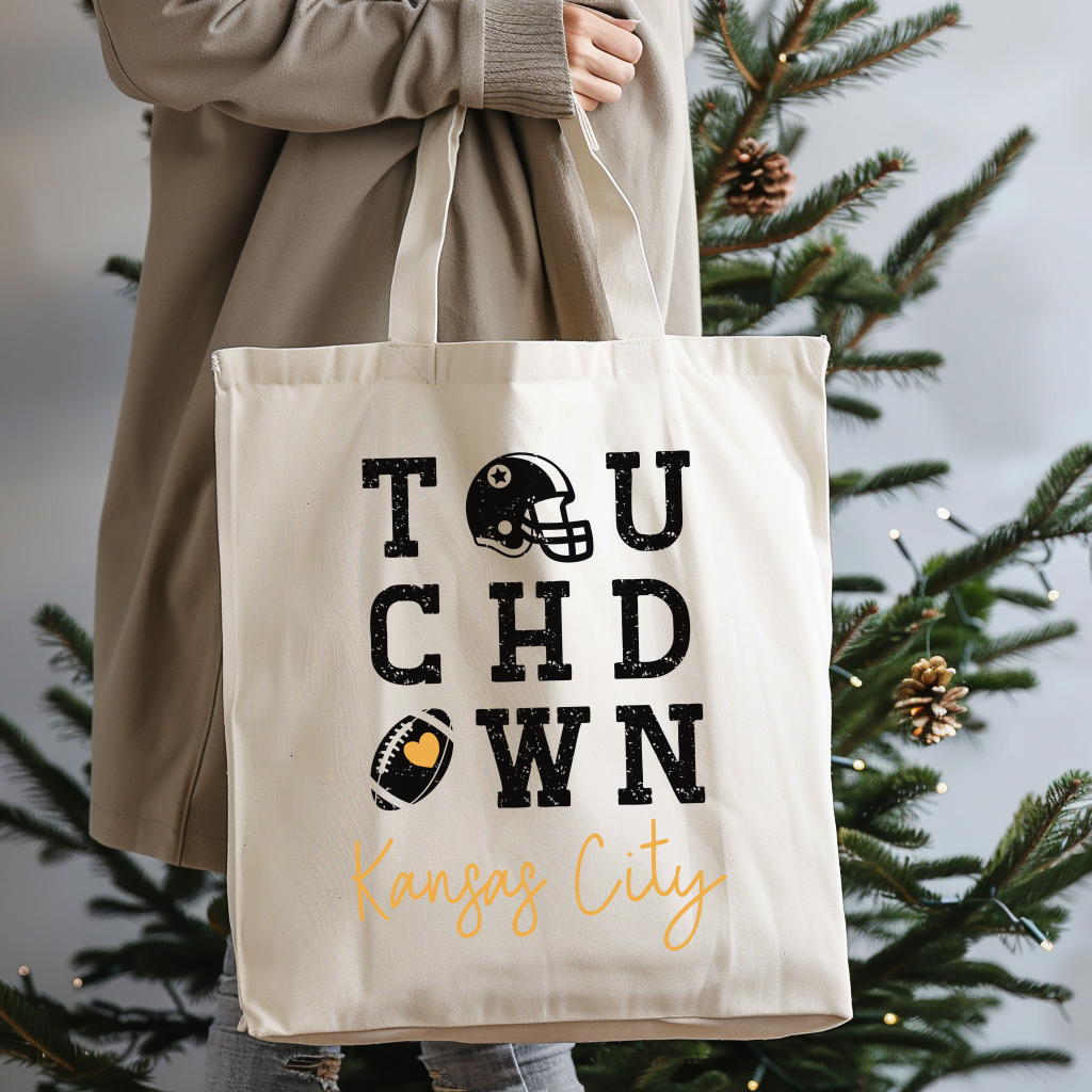 Tote bag with 'Touchdown Kansas City' text held by a person in front of a Christmas tree.