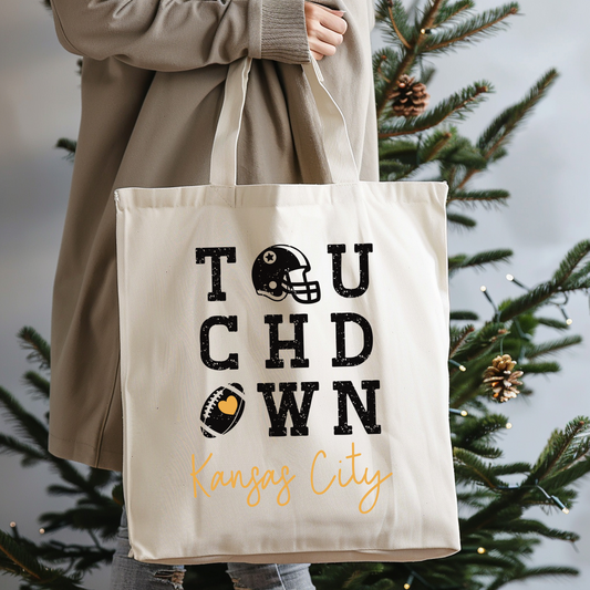 Tote bag with 'Touchdown Kansas City' text held by a person in front of a Christmas tree.