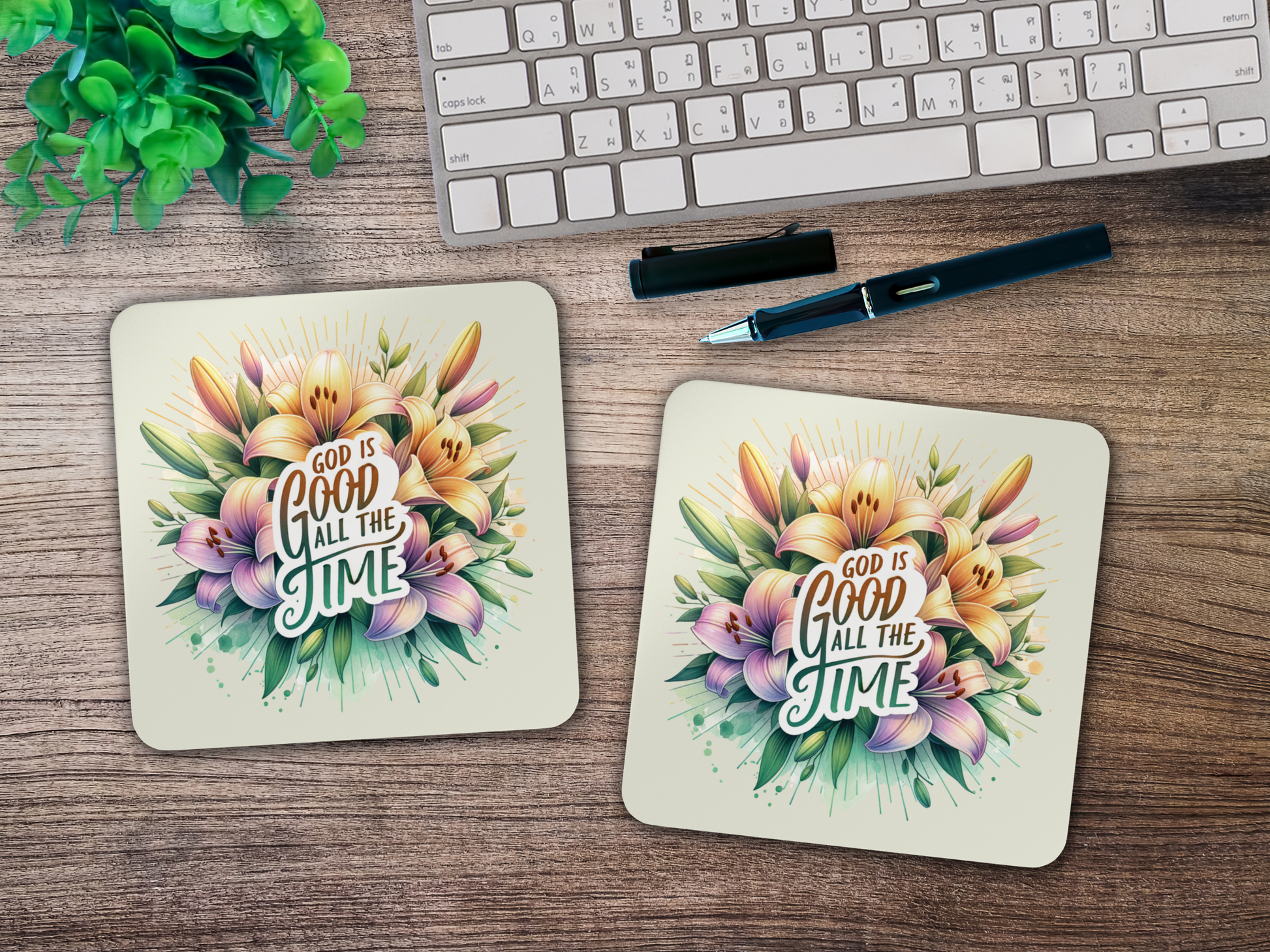 Pair of scripture coasters with vibrant floral artwork styled on a wooden desk beside keyboard, pen, and green plant.