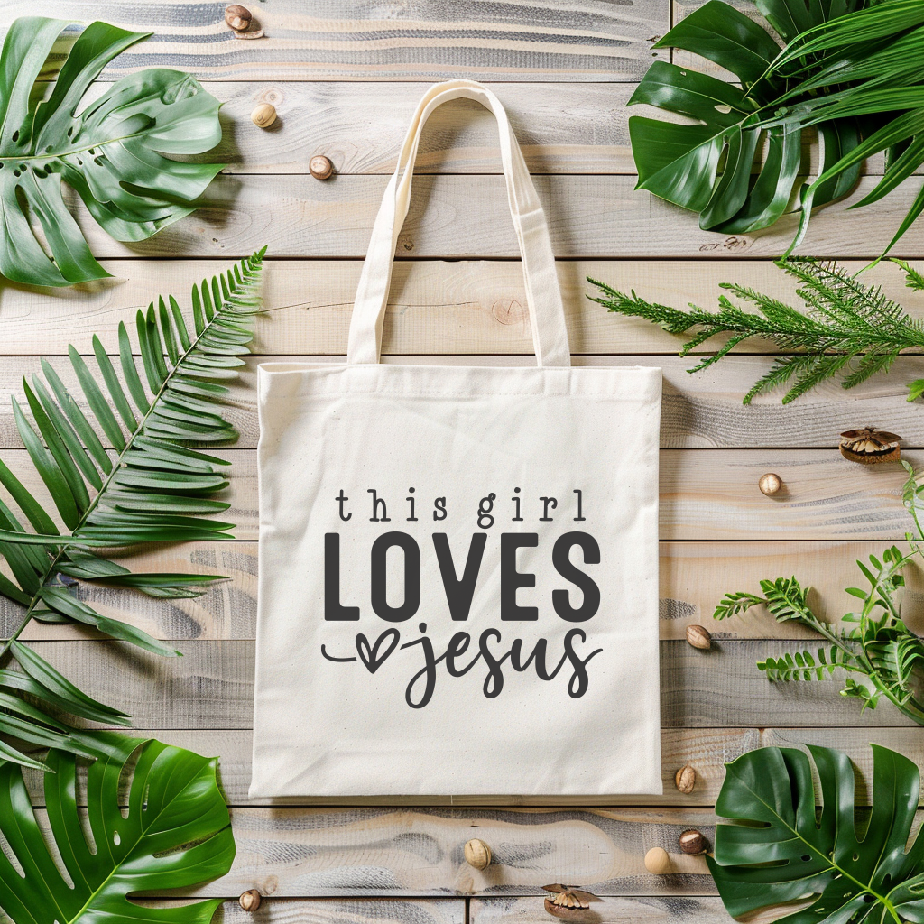 Tote bag with 'this girl LOVES Jesus' text on a wooden surface with leaves