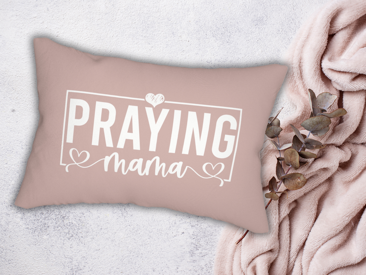 Inspirational Christian pillow reading “Praying Mama,” displayed on textured surface with blush throw blanket and eucalyptus leaves.