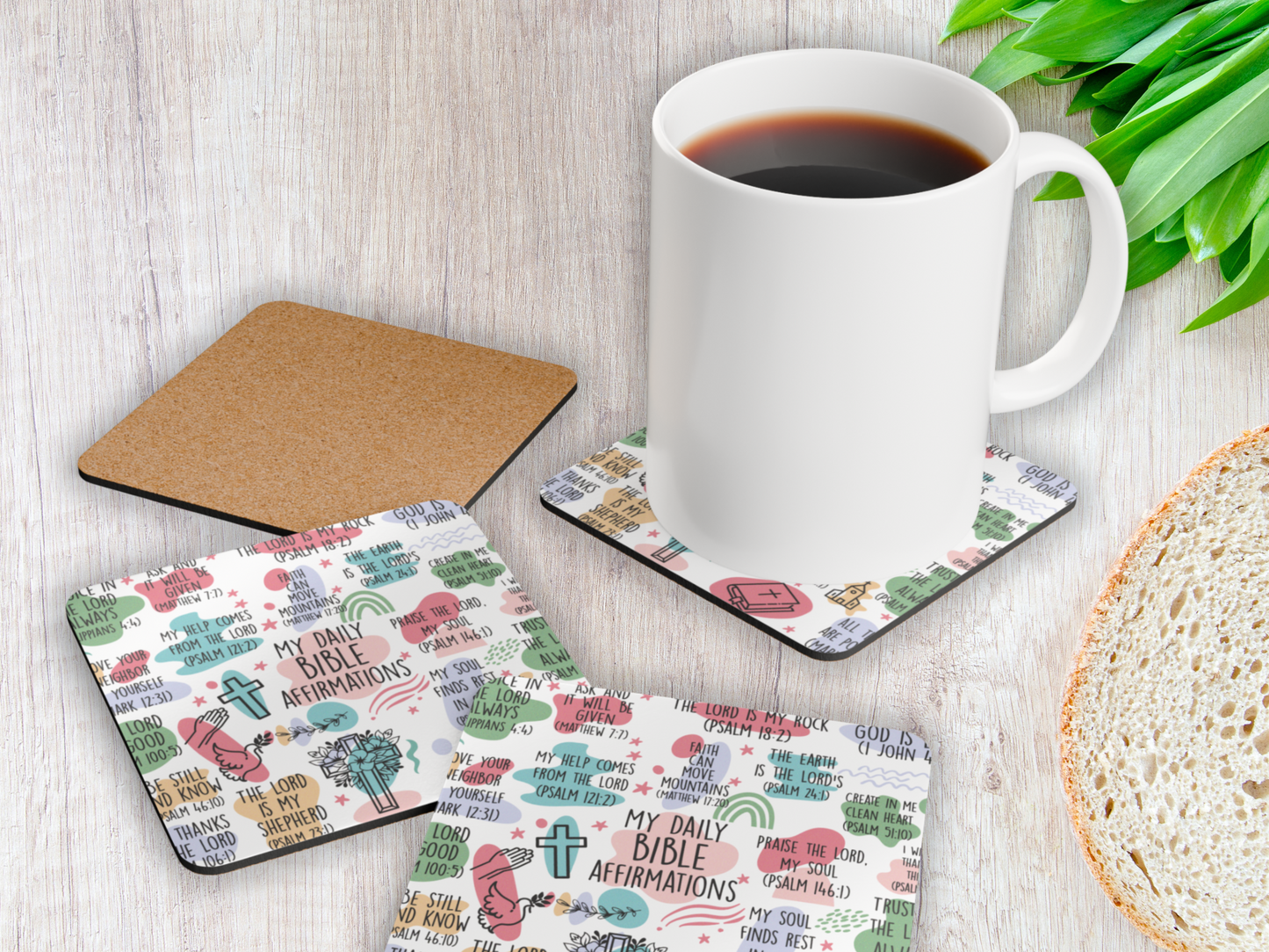 Christian scripture coasters displayed with a coffee mug and bread slice on rustic white wooden table with greenery.