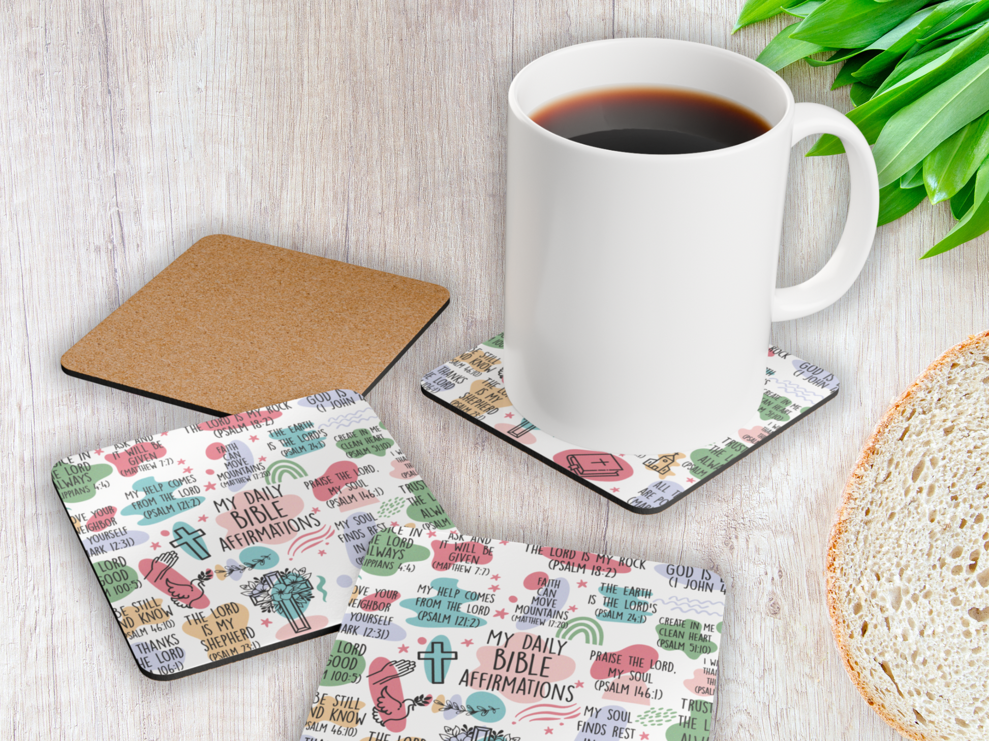 Christian scripture coasters displayed with a coffee mug and bread slice on rustic white wooden table with greenery.
