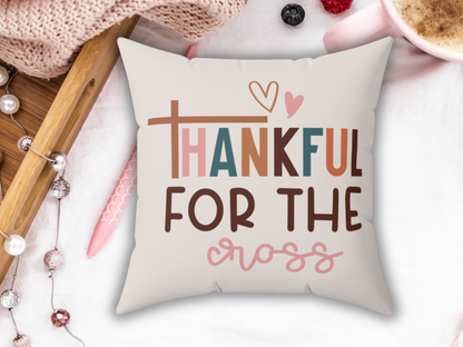 A decorative pillow with the text "Thankful for the Cross" in colorful letters, featuring a heart design. Set on a cozy blanket with festive ornaments.