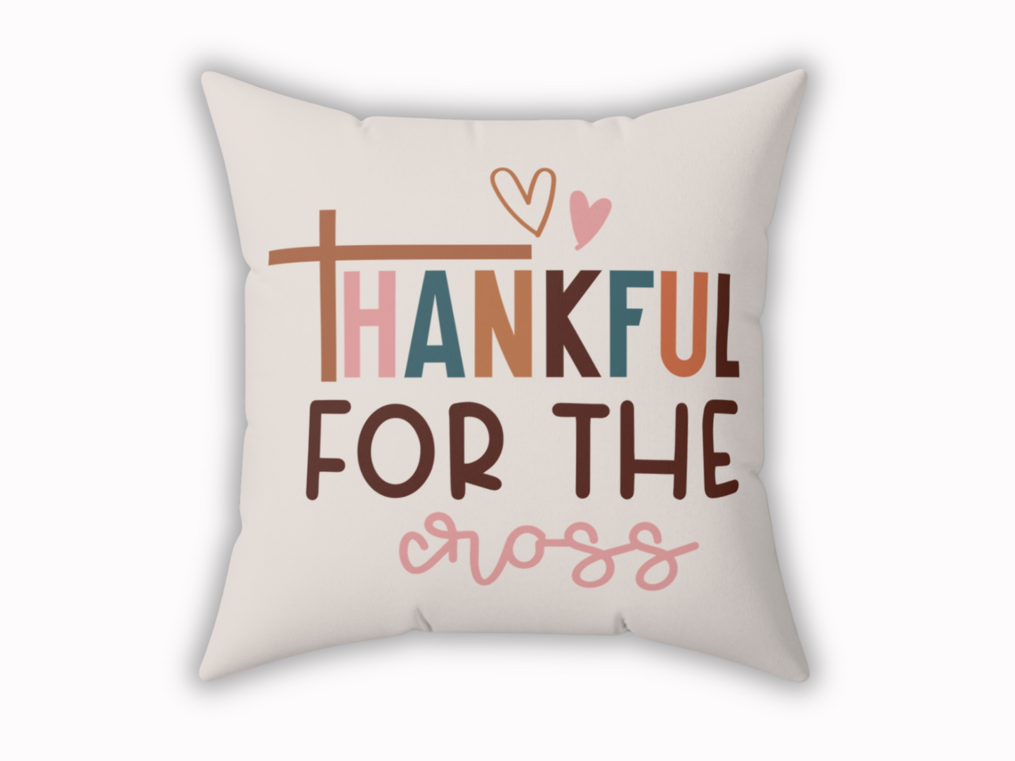 A beige decorative pillow with the phrase "Thankful for the Cross" in colorful, bold letters. Features a heart above and a cross symbol as the letter "T."