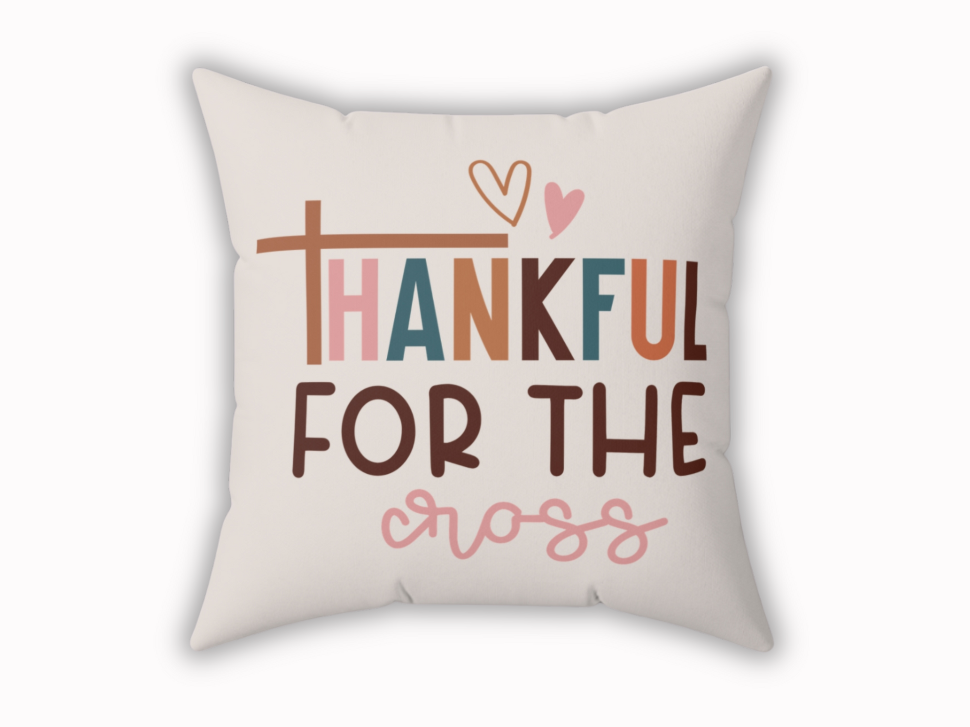 A beige decorative pillow with the phrase "Thankful for the Cross" in colorful, bold letters. Features a heart above and a cross symbol as the letter "T."