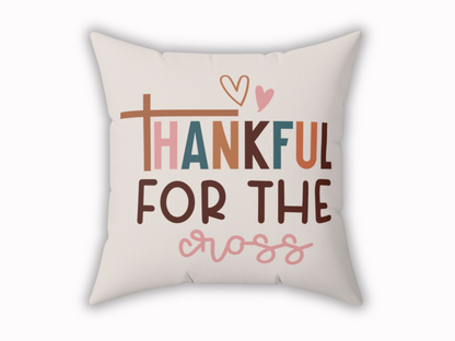 A beige decorative pillow with the phrase "Thankful for the Cross" in colorful, bold letters. Features a heart above and a cross symbol as the letter "T."