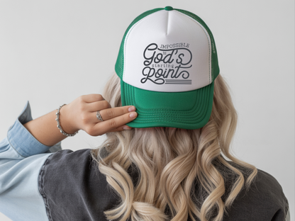 Person wearing a green and white cap with text, holding it on a plain background