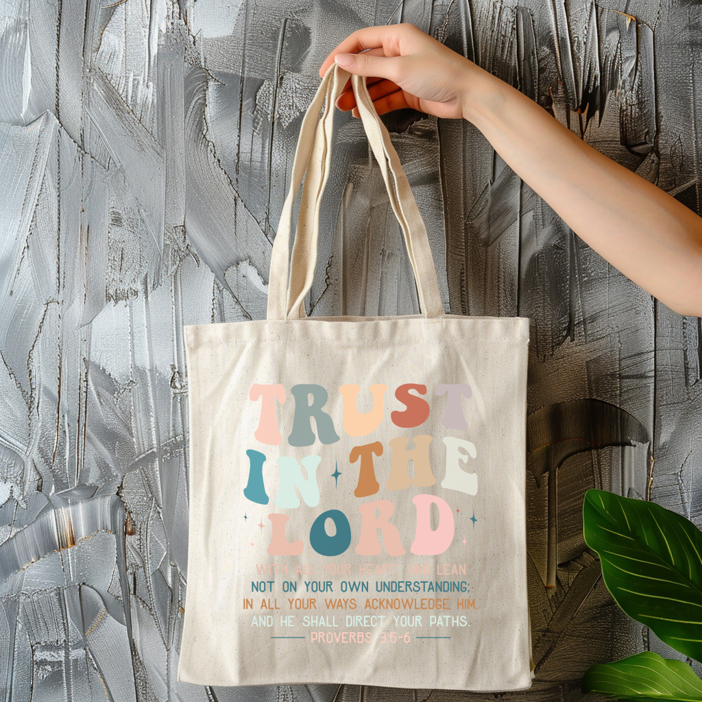 Tote bag with 'Trust in the Lord' text held by a hand against a textured wall.