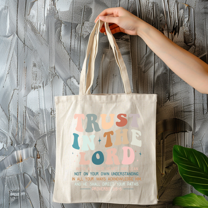 Tote bag with 'Trust in the Lord' text held by a hand against a textured wall.