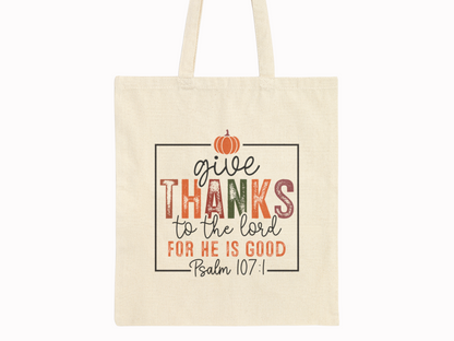 Canvas tote bag with "Give thanks to the Lord for He is good, Psalm 107:1" in colorful letters. A small orange pumpkin decorates the top.